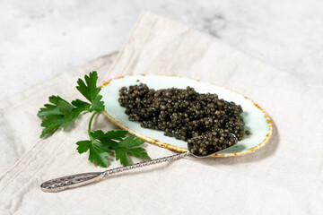 Black caviar. Black sturgeon caviar in a ceramic bowl and a metal spoon on a light background. Useful delicacy	