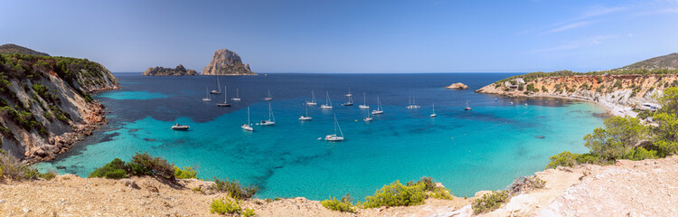 Fototapeta na wymiar Beautiful Panorama of bay Cala Hort with sea sailing yachts and the mountain Es Vedra. Ibiza, Balearic Islands, Spain