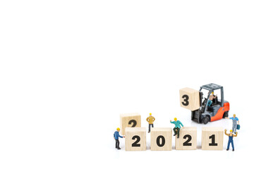 miniature worker team building standing front of forklift machine with white 2021 number on wooden block on white background.