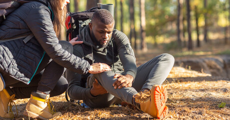 Fototapeta premium Unrecognizable woman comforting injured black guy, backpacking together by forest