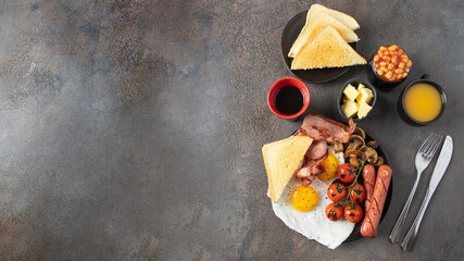 Top view of Full English breakfast  on concrete background.  Fried eggs, sausages, bacon, beans, mushrooms, toasts, butter, coffee, juice