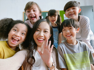 Smiling young Asian teacher making selfie with her schoolchildren in classroom. Elementary school,technology, children and people concept