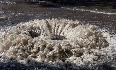 Water flows out of drainage hatch. Drainage fountain of sewage. Accident in sewage system. Dirty...