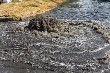 Water flows out of drainage hatch. Drainage fountain of sewage. Accident in sewage system. Dirty sewer water flows fountain on road. Drainage system for wastewater discharge does not work
