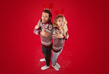 Full length portrait of young couple in Christmas sweaters shivering over red background, above view