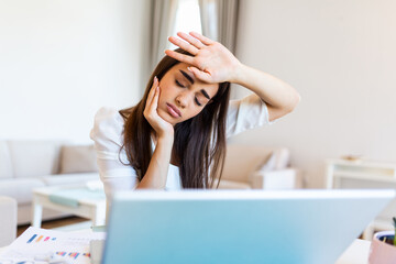 Young frustrated woman working from home office in front of laptop with fever checking her...