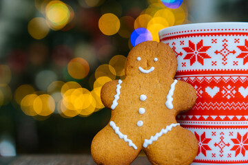 Christmas postcard with gingerbread man red mug with christmas ornament on light bokeh from Xmas tree and red striped holidays candies. Xmas candies and cup with marshmallow on wood background