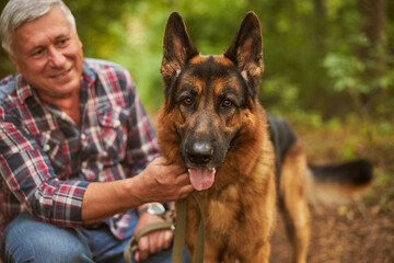 Aging man posing with his german shepherd in the woods