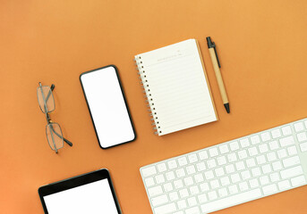 Top view of modern smartphone, tablet and white headphones on orange color background.