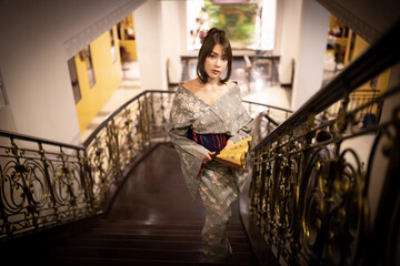 A beautiful Asian woman in traditional Japanese kimono, standing on the stairs and looking at the...