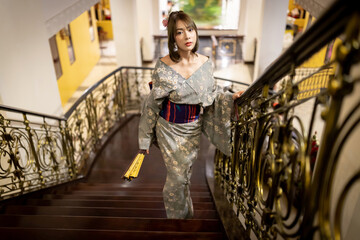 A beautiful Asian woman in traditional Japanese kimono, standing on the stairs and looking at the...