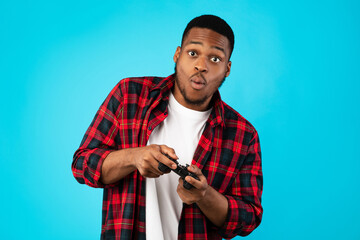 Black Millennial Guy Playing Video Games Standing Over Blue Background © Prostock-studio