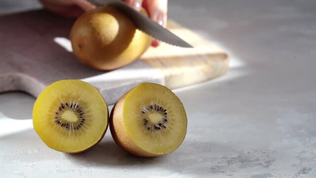 Cutting yellow kiwi halves on gray background.