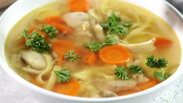 Homemade chicken soup with noodles and vegetables in white bowl, white background. Healthy warm comfortable food.