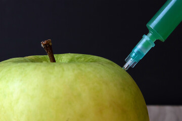 Green apple on a wooden board and syringe inside it extracting green liquid