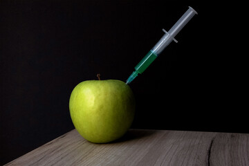 Green apple on a wooden board and syringe inside it extracting green liquid