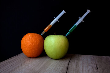 Bright orange and green apple on a wooden board and syringes extracting liquid from them