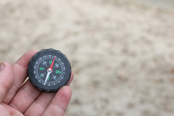 classic navigation compass in hand in summer against background of sandy beach as symbol of tourism...