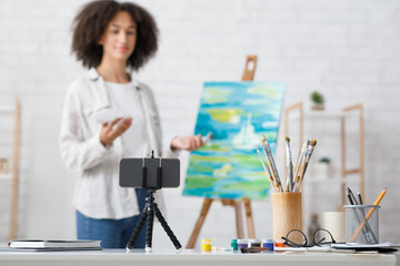 Smartphone with tripod close up. Woman draws picture in studio interior blurry