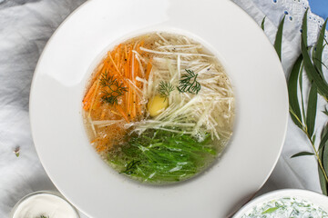 chicken broth with egg with carrot and cabbage on white plate on the table at restaurant