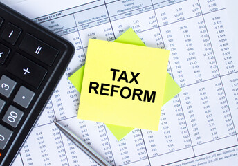 Sticker with text Tax Reform lying on the financial tables. Calculator with metal pen