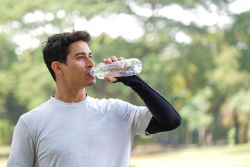 Portrait of a young man drinking water in park after running in the morning