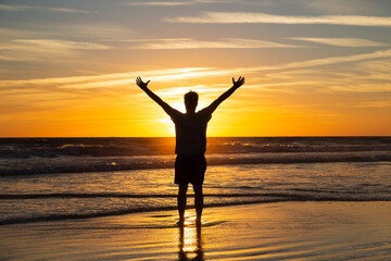 Fototapeta na wymiar Man silhouette with his hands up in the long beach of Zahara de los Atunes in the Atlantic Ocean at sunset, Cadiz, Spain