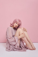 Woman with dyed pink hair in a long dress is sitting on the floor. Portrait of a girl with hair coloring at the pink wall. Perfect hairstyle and hair styling