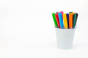 Set multicolored pointed markers in a white metal bucket on light background, copy space. Drawing felt-tip pens, pencils, artists tools, creativity, leisure, hobby. Colorful school supplies.