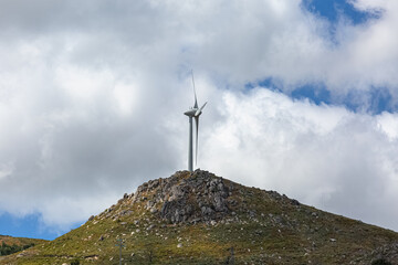 View of a wind turbines on top of mountains, dirt road and wild nature and landscape, cloudy sky as background