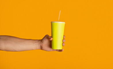 Male hand holding disposable cup with refreshing summer drink on orange background, closeup