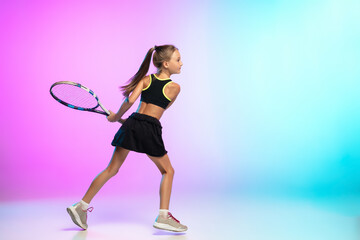Running high. Little tennis girl in black sportwear isolated on gradient background in neon light. Little caucasian model, sport kid training in motion and action. Sport, movement, childhood concept.