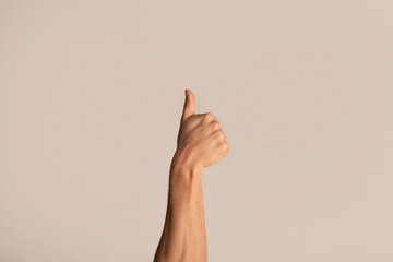 Cropped view of young guy showing thumb up gesture, expressing approval on light background