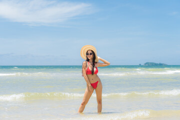 Fototapeta na wymiar Asian woman wear a colourful bikini stand sunbathing on the sandy beach in a bright day and happy holidays with blue sky 