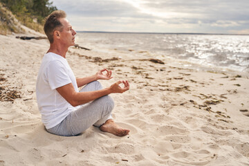 Mature man meditating in morning in beach