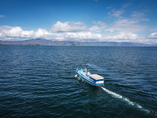 Naklejka premium Aerial view of a steamboat, A fishing ship in the middle of a lake with beautiful coastline behind