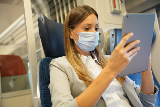 Businesswoman Commuting By Train, Working On Digital Tablet And Wearing Face Mask