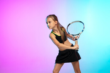 Obraz na płótnie Canvas Powerful. Little tennis girl in black sportwear isolated on gradient background in neon light. Little caucasian model, sport kid training in motion and action. Sport, movement, childhood concept.