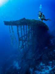 Eine weibliche Taucherin taucht vor einem alten, versunkenen Schiffswrack im tiefen blau der Ägäischen See, Griechenland