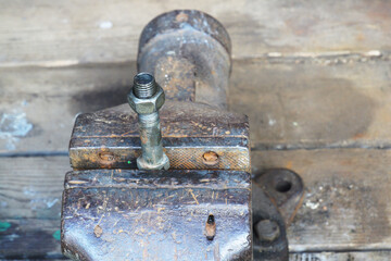 A bolt with a screwed nut is clamped in a large locksmith's vice.