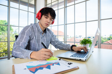 young asian businessman wear headphones study online watching webinar podcast on laptop listening learning business course on website.