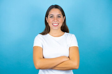 Young beautiful woman over isolated blue background smiling with her arms crossed