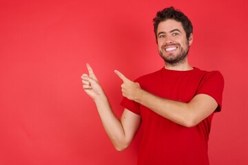 Young handsome caucasian man wearing t-shirt over isolated red background indicating with...