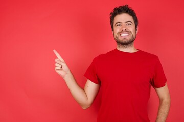 Young handsome caucasian man wearing t-shirt over isolated red background looking indicating fingers hands side empty space advising novelt