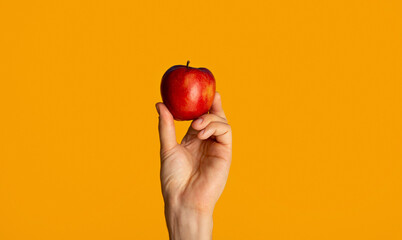 Male hand showing yummy red apple on orange background