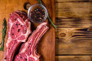 Raw ribeye steak, glass jar with spices and rosemary on cutting board. Top view