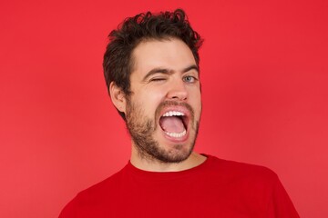 Young handsome caucasian man wearing t-shirt over isolated red background winking looking at the camera with sexy expression, cheerful and happy face.