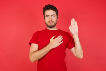 Young handsome caucasian man wearing t-shirt over isolated red background Swearing with hand on...