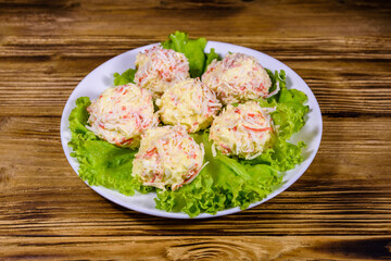 White plate with crab-cheese balls and lettuce leaves on wooden table