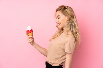Young blonde woman holding a cornet ice cream isolated on pink background with happy expression